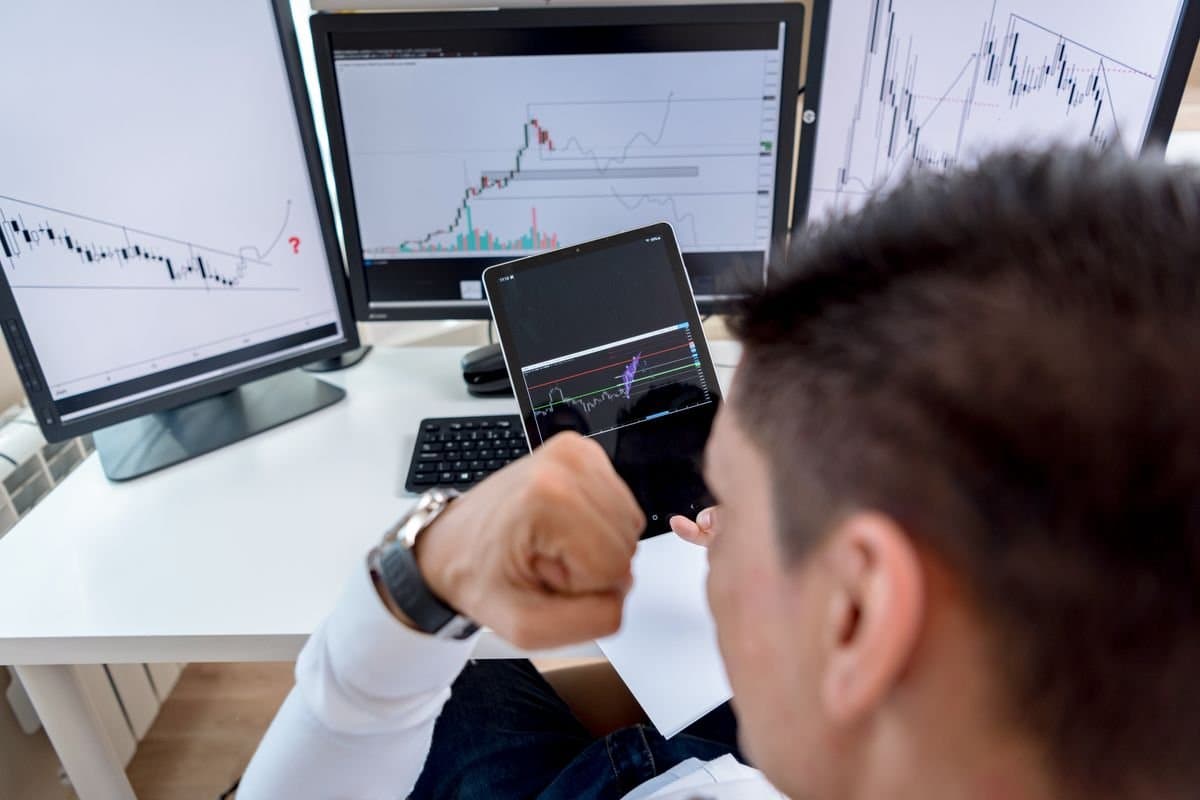 Confident trader viewing stock market charts across multiple monitors